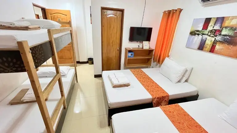 Room with two single beds and a wooden bunk bed, orange curtains, wall art, and a small TV on a shelf